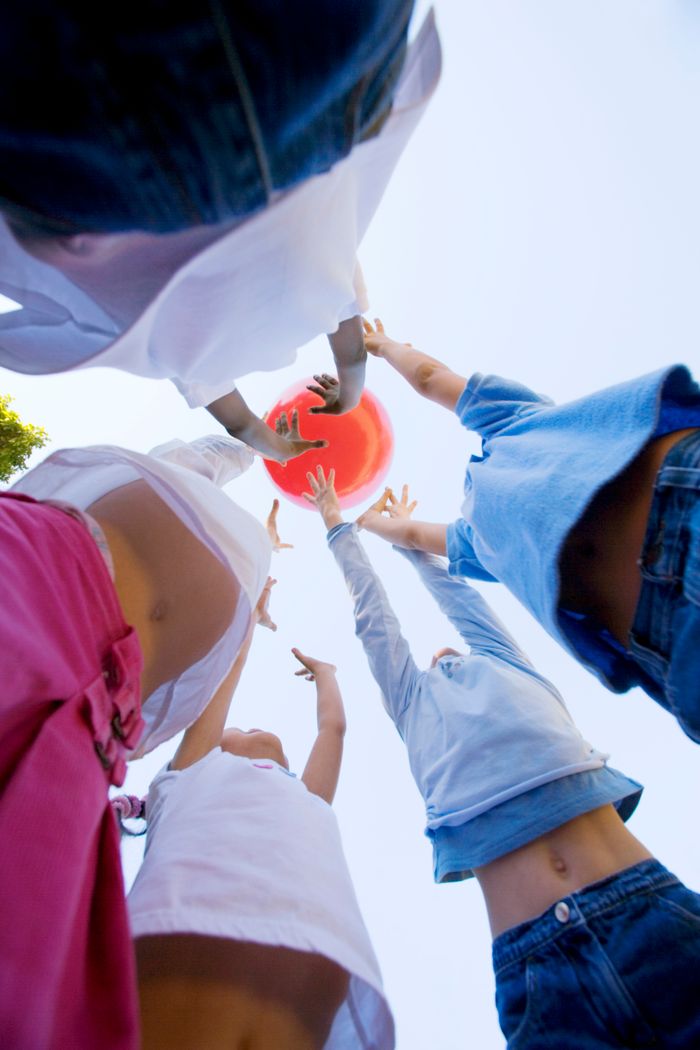 Dynamic low-angle shot of kids reaching for a ball outdoors.